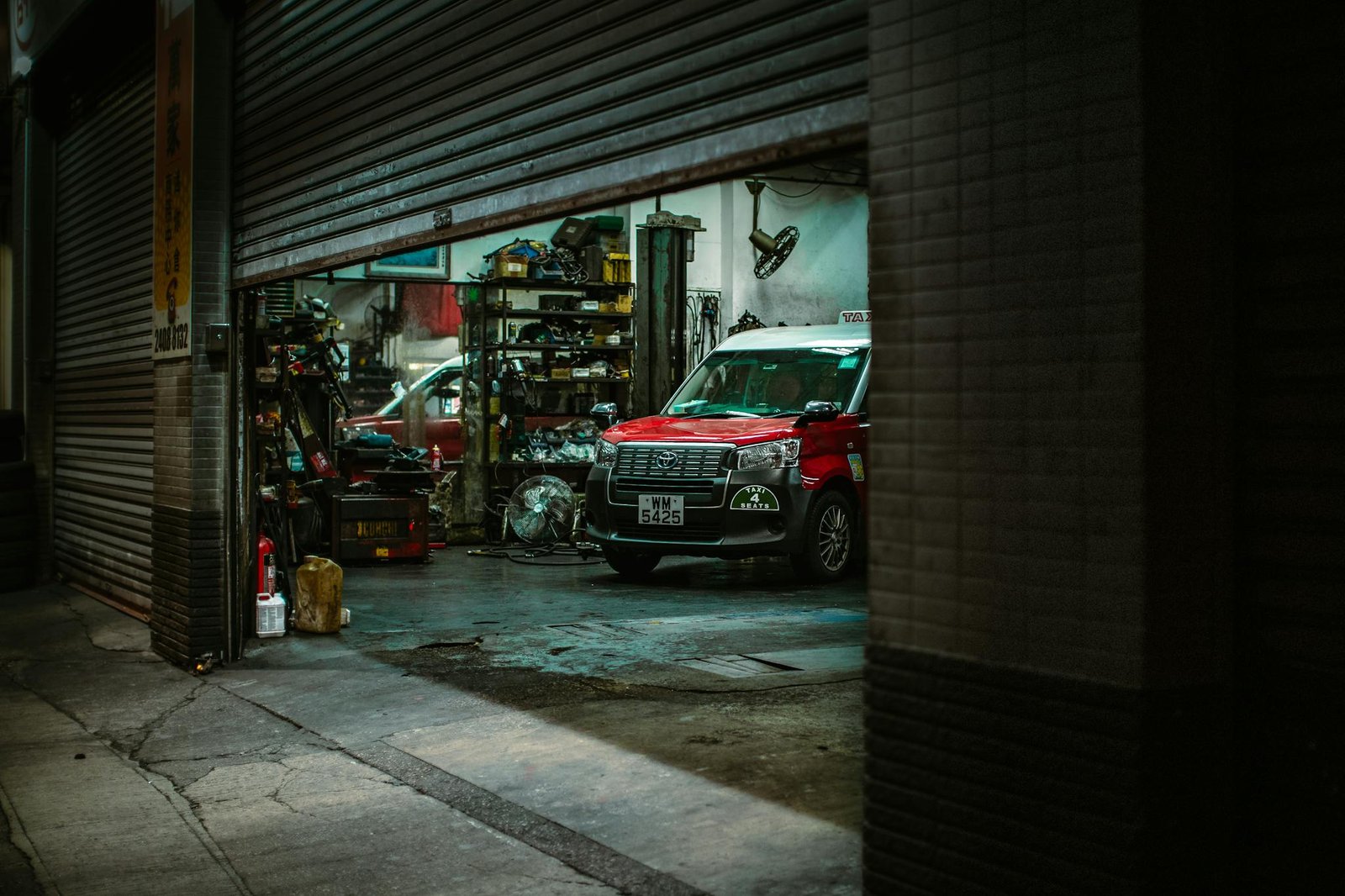 Red car inside a Hong Kong auto repair shop with open roller shutter, showcasing tools and equipment.